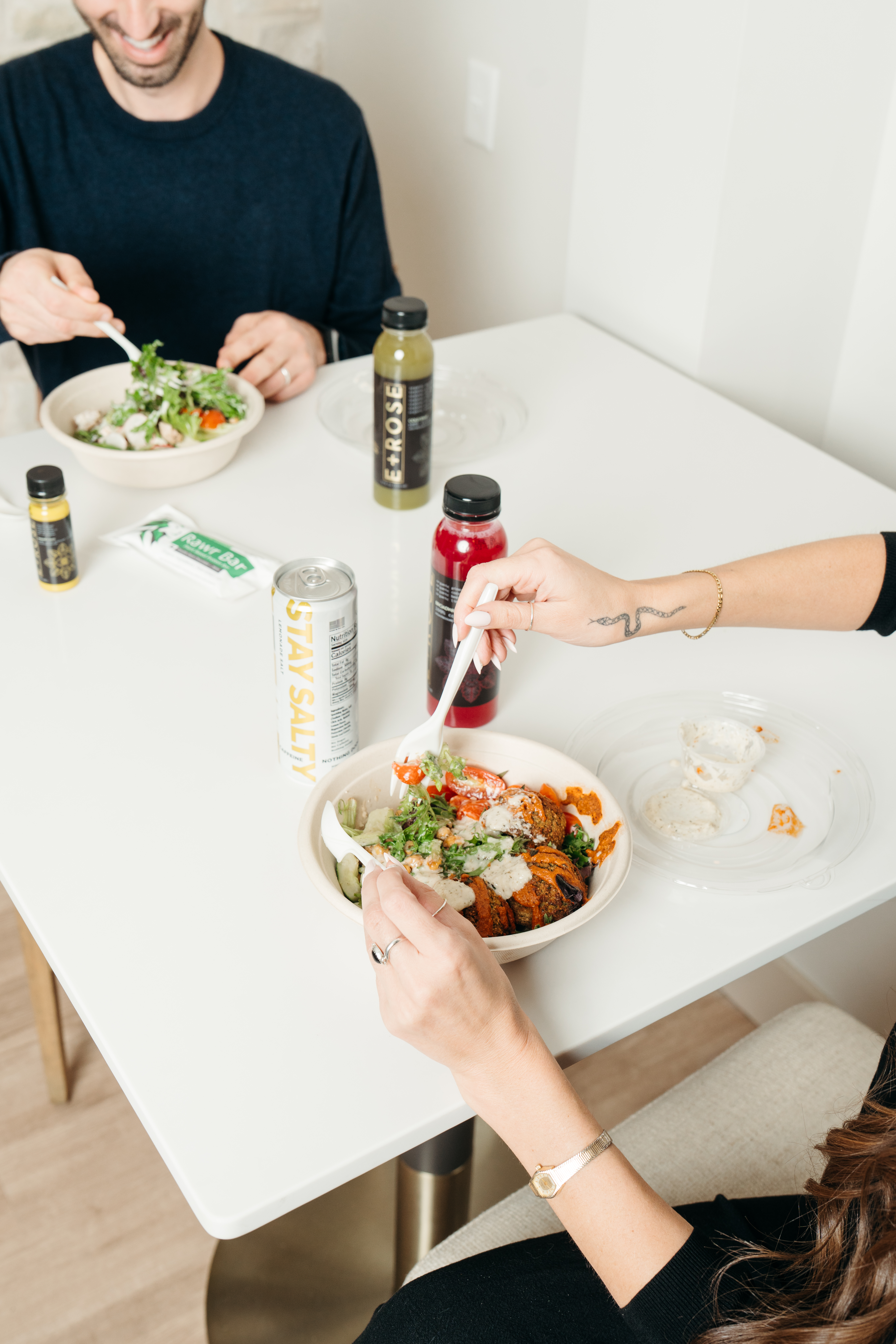 Two people sit at a table eating healthy salad bowls.
